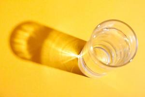 Glass of water on orange background with shadow. photo