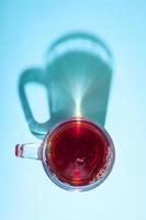 Glass of tea on blue background under the bright sunlight with creative shadow.
