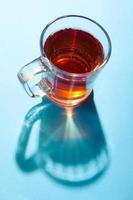 Glass of tea on blue background under the bright sunlight with creative shadow.