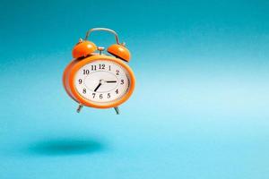 Orange vintage style flying alarm clock. Flying alarm clock on blue background.