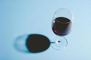 Copa de vino tinto sobre fondo azul con sombra oscura. foto