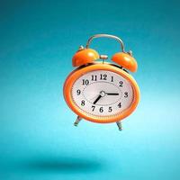 Orange vintage style flying alarm clock. Flying alarm clock on blue background. photo