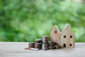 Money coin stack and wooden house over blurred green garden background, saving money and business financial management concept. photo