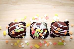 deliciosa bola de pastel de chocolate de postre dulce con cobertura colorida en una taza de papel de aluminio sobre tabla de madera. foto