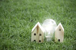 Wooden house and light bulb on green grass, energy-saving, using renewable green energy for saving the world, love and protect our planet, environmental friendly concept photo