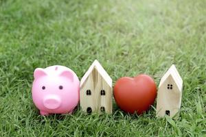 Pink piggy bank, red heart and wooden house on green grass, save money for a house photo