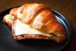 Freshly baked homemade delicious croissant sandwich ham cheese in black plate on wooden breakfast table. photo