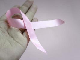 Hands holding breast cancer awareness pink ribbon on pink background, october symbol, healthcare and medicine concept photo