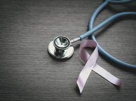cinta rosa de concienciación sobre el cáncer de mama con estetoscopio médico sobre fondo de madera, símbolo de octubre, concepto de salud y medicina foto