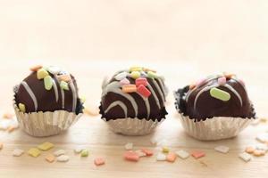 Delicious fancy sweet dessert chocolate cake ball with colorful topping in aluminium foil cup on wooden board.