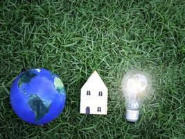 Earth, wooden house and light bulb on green grass, energy-saving, using renewable green energy for saving the world, love and protect our planet, environmental  friendly concept photo