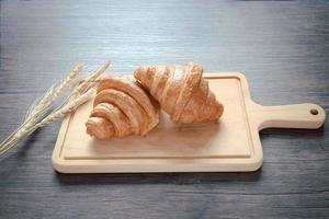 Two freshly baked delicious croissants with spikelets on wooden cutting board, food on breakfast table photo
