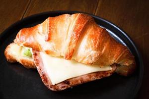 Freshly baked homemade delicious croissant sandwich ham cheese in black plate on wooden breakfast table, top view of breakfast table.