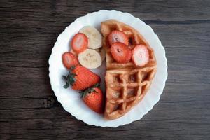 Viennese waffles with strawberry and banana in white plate on dark table. photo