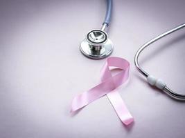 cinta rosa de concientización sobre el cáncer de mama con estetoscopio médico sobre fondo rosa, símbolo de octubre, concepto de salud y medicina foto