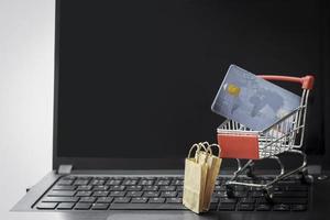 Credit card in trolley on laptop keyboard with shopping bags. Online shopping, electronic commerce business and buying goods from seller over the internet concept photo