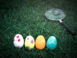 huevos de pascua coloridos sobre hierba verde con lupa, cazador de huevos de pascua foto