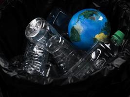 Earth globe is thrown into trash bin with  plastic rubbish waste,  Earth day, ecology and environment concept photo