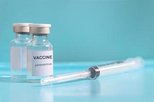 Glass vials contain liquid medical vaccine used to shot for injection treatment with blurred needle syringe on blue background and copy space, vaccination and immunization care for preventing virus