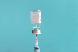 Medical needle syringe entering into glass via that containing liquid medical vaccine used to shot for injection treatment on blue background, vaccination and immunization care concept. photo