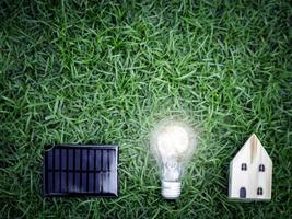 Solar cell, light bulb and wooden house on green grass, energy-saving, using renewable green energy for saving the world, love and protect our planet, environmental friendly concept photo