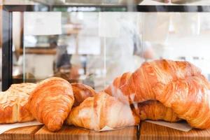 Freshly baked delicious croissants lying in display glass cabinet of bakery shop.