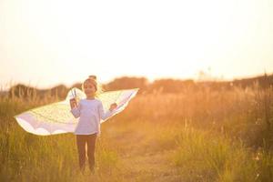 Girl is standing with wings in field, learning to fly a kite . Outdoor entertainment in summer, nature and fresh air. Childhood, freedom and carelessness. Children's dreams and hope