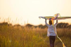 A girl runs into a field with a kite, learns to launch it. Outdoor entertainment in summer, nature and fresh air. Childhood, freedom and carelessness. A child with wings is a dream and a hope. photo