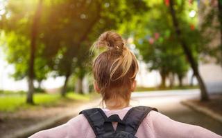 A little girl of Caucasian in a school uniform with a backpack looks at the road in the school yard. Concept back to school. Elementary school, developing activities for preschoolers. Space for text photo