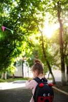 una niña caucásica con uniforme escolar y mochila mira la carretera en el patio de la escuela. concepto de regreso a la escuela. primaria, desarrollando actividades para preescolares. espacio para texto foto