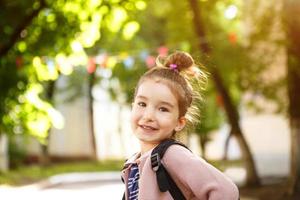 A little girl of Caucasian appearance in a school uniform with a backpack looks into the frame. Concept back to school. The first class, developing activities for preschoolers. Space for text