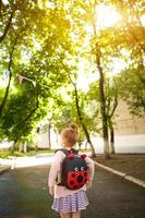A little girl of Caucasian in a school uniform with a backpack looks at the road in the school yard. Concept back to school. Elementary school, developing activities for preschoolers. Space for text photo