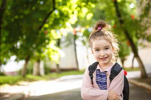 A little girl of Caucasian appearance in a school uniform with a backpack looks into the frame. Concept back to school. The first class, developing activities for preschoolers. Space for text