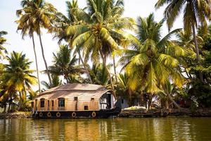 House-boat pleasure cruise ship in India, Kerala on the seaweed-covered river channels of Allapuzha in India. Boat on the lake in the bright sun and palm trees among the tropics. Sight Houseboat photo