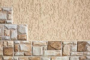 Stone tiles in the form of steps made of rectangular fragments of beige and sand color and plaster on the wall with a bark beetle pattern. Background, texture. Exterior decoration of building, house. photo