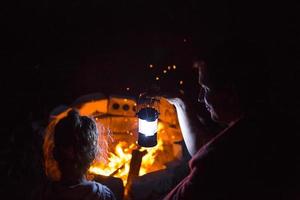 papá e hija se sientan por la noche junto al fuego al aire libre en verano en la naturaleza. viaje de campamento familiar, reuniones alrededor de la fogata. día del padre, barbacoa. linterna de camping y carpa foto