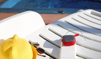 Music portable speaker is charged from the power bank via usb on a deck chair near the pool with beach accessories. Always in touch, travel gadgets, external battery for a smartphone. Place for text. photo