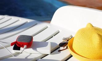 Music portable speaker is charged from the power bank via usb on a deck chair near the pool with beach accessories. Always in touch, travel gadgets, external battery for a smartphone. Place for text. photo