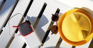 Music portable speaker is charged from the power bank via usb on a deck chair near the pool with beach accessories. Always in touch, travel gadgets, external battery for a smartphone. Place for text. photo