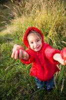 A little girl in a red jacket with a hood holds out apples in her hands. Autumn harvest festival, thanksgiving, orchard, vitamins. Space for text