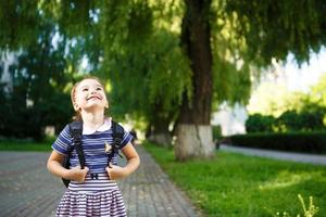 A little girl of Caucasian appearance in a school uniform with a backpack and the book. Concept back to school. Elementary school, developing activities for preschoolers. Space for text photo