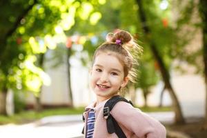 una niña de apariencia caucásica con uniforme escolar y mochila mira hacia el marco. concepto de regreso a la escuela. la primera clase, desarrollando actividades para preescolares. espacio para texto foto