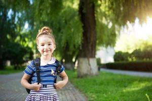 A little girl of Caucasian appearance in a school uniform with a backpack looks into the frame. Concept back to school. Elementary school, developing activities for preschoolers. Space for text photo