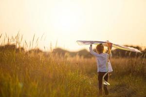 una niña corre a un campo con una cometa, aprende a lanzarla. animación al aire libre en verano, naturaleza y aire puro. infancia, libertad y despreocupación. un niño con alas es un sueño y una esperanza. foto