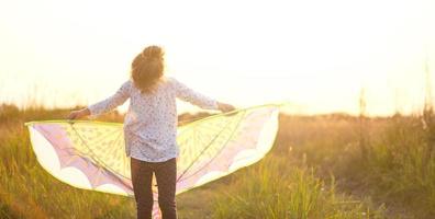 Girl is standing with wings in field, learning to fly a kite . Outdoor entertainment in summer, nature and fresh air. Childhood, freedom and carelessness. Children's dreams and hope photo