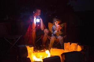 Dad and daughter sit at night by the fire in the open air in the summer in nature. Family camping trip, gatherings around the campfire. Father's Day, barbecue. Camping lantern and tent photo