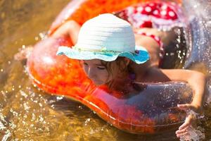 chica con sombrero nadando en el río con un círculo inflable transparente en forma de corazón con plumas naranjas dentro.el mar con un fondo arenoso. vacaciones en la playa, nadar, broncearse, protectores solares. foto