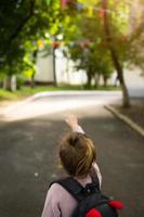 A little girl of Caucasian in a school uniform with a backpack looks at the road in the school yard. Concept back to school. Elementary school, developing activities for preschoolers. Space for text photo