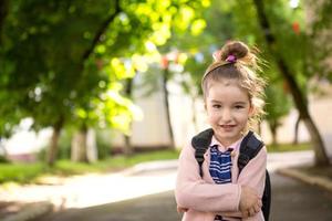 A little girl of Caucasian appearance in a school uniform with a backpack looks into the frame. Concept back to school. Elementary school, developing activities for preschoolers. Space for text photo