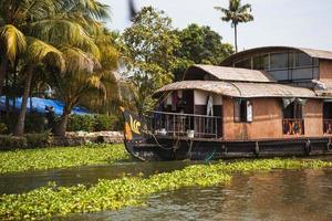 House-boat pleasure cruise ship in India, Kerala on the seaweed-covered river channels of Allapuzha in India. Boat on the lake in the bright sun and palm trees among the tropics. Sight Houseboat photo